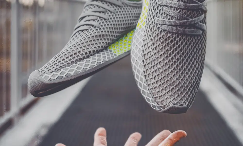 Bild von grauen Laufschuhen in der Luft mit Maennerhand und Laufstrecke Asphalt im Hintergrund